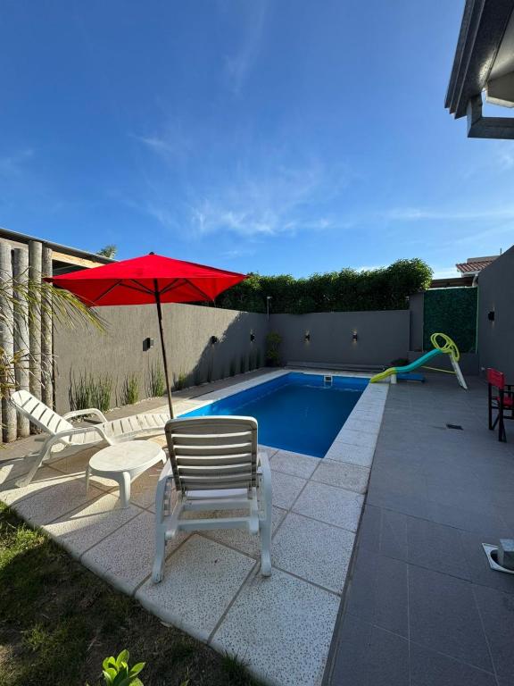 a patio with a red umbrella and chairs and a pool at Casa 109 in Necochea