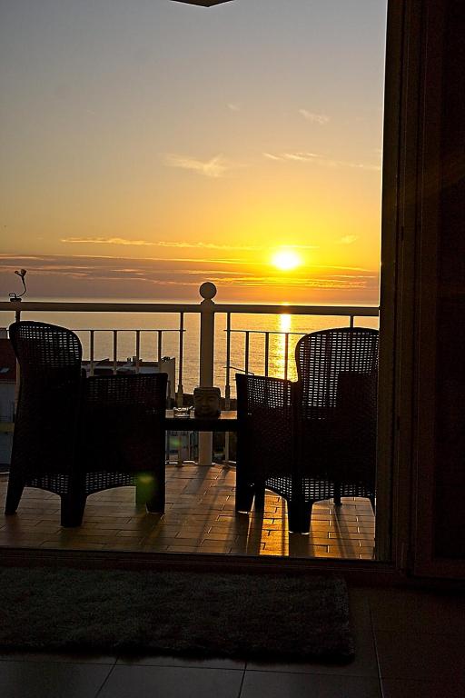 a sunset on a balcony with chairs and a table at Ericeira Sunset Apartment in Ericeira