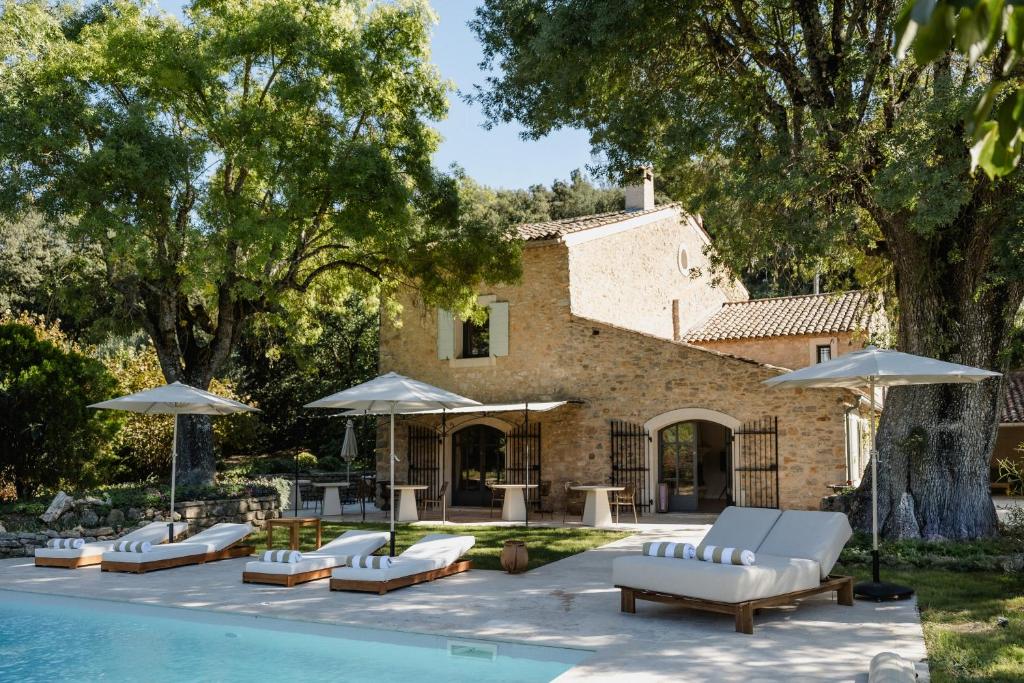 a pool with lounge chairs and umbrellas next to a house at La Bastide de Monique - Maison d'hôtes en Provence in Flassans-sur-Issole