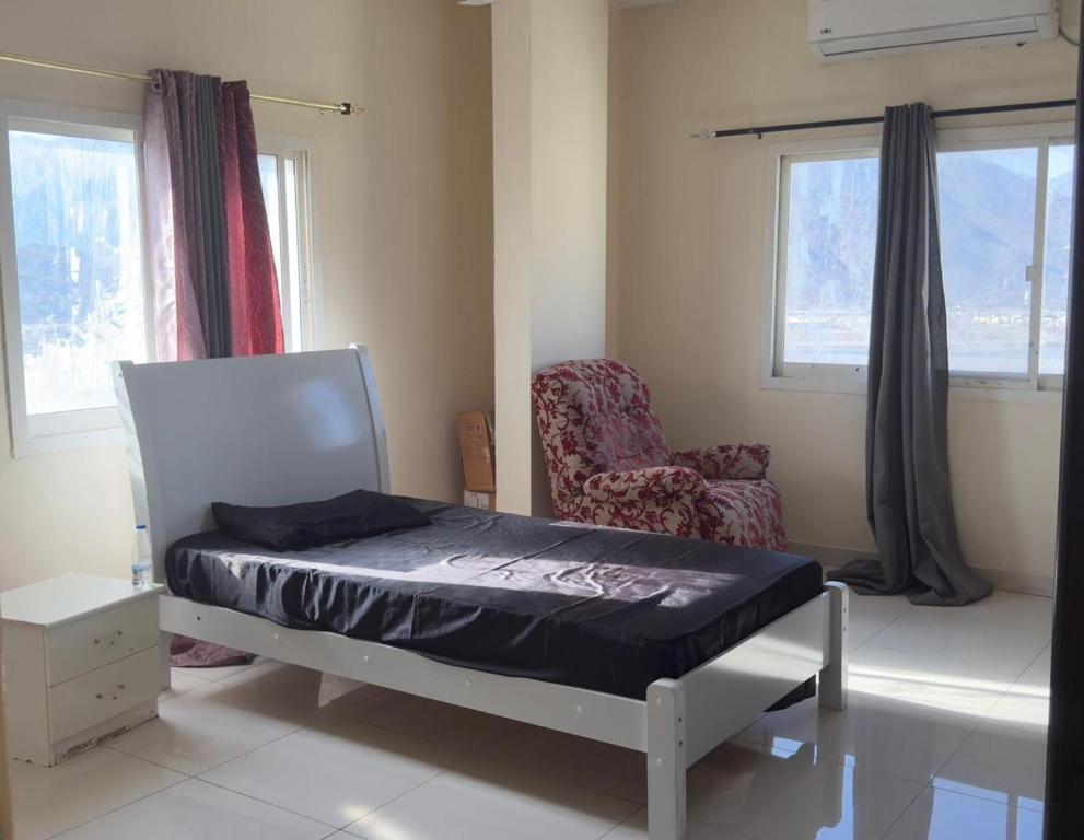 a bedroom with a bed and a chair and window at Stay home in ‘Uqayr