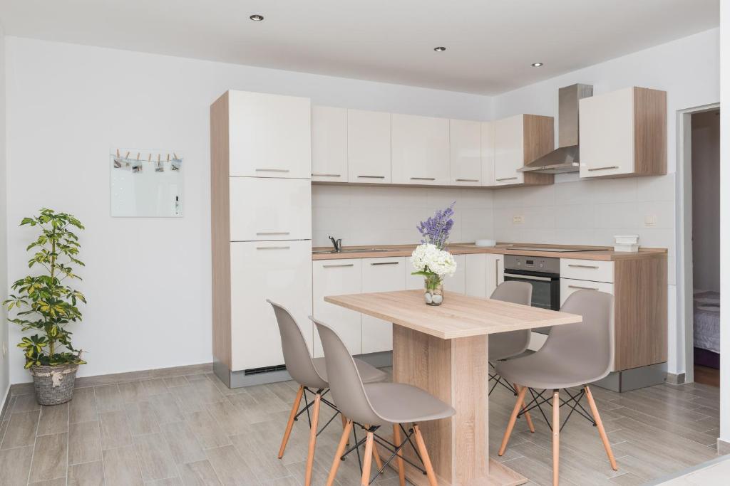 a kitchen with white cabinets and a wooden table and chairs at Apartmani Španja in Vodice