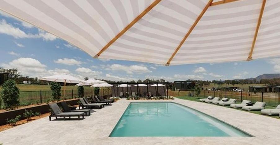 a swimming pool with a large umbrella and chairs at The Lane Retreat in Pokolbin