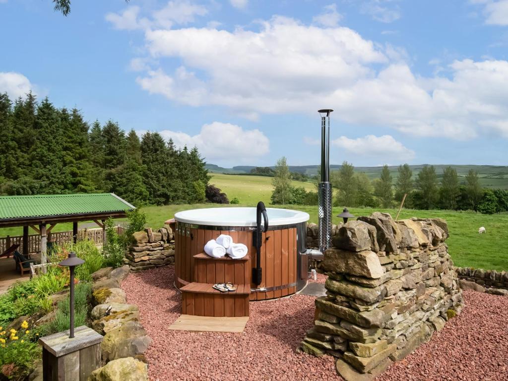 een hot tub in een tuin naast een stenen muur bij Broomstick Cottage in Elsdon