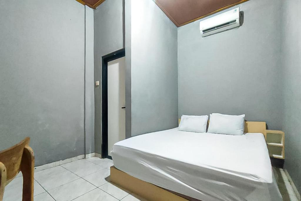 Un dormitorio con una cama blanca y una silla. en Nay Guesthouse near UMS Mitra RedDoorz, en Colomadu