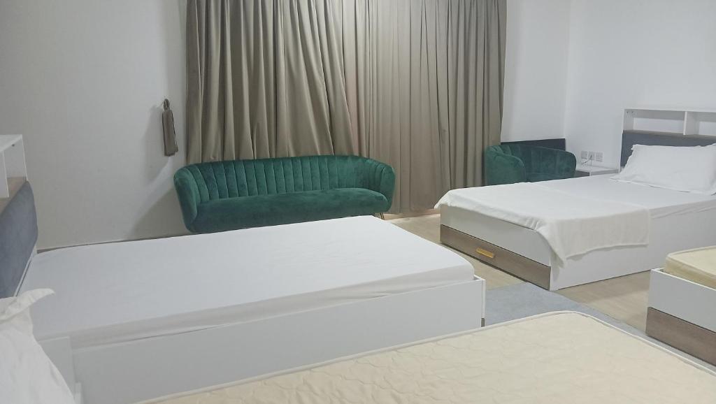a hotel room with two beds and a green chair at Private Rooms And Bed Spaces Available In Sohar in Al ‘Awhī