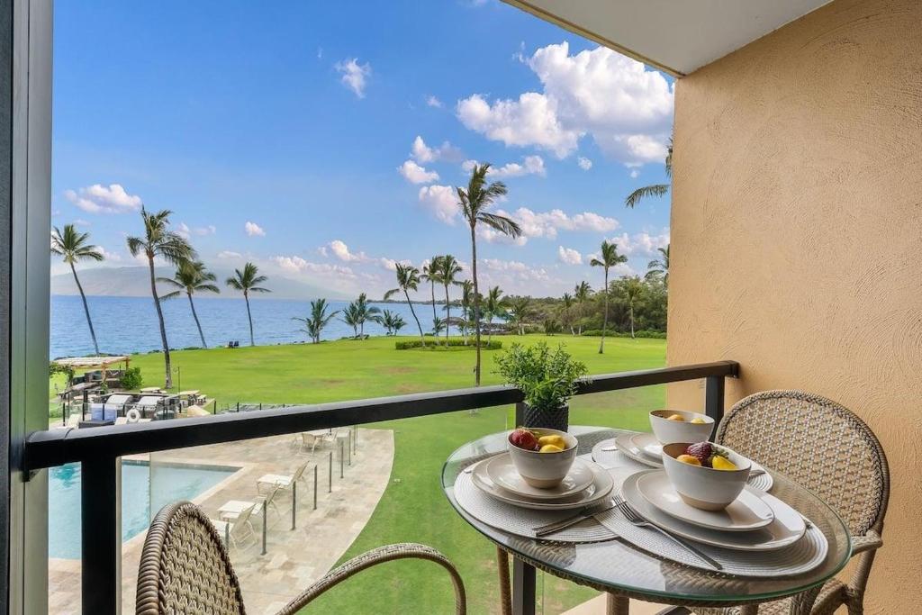 a table with two cups on a balcony with a view of the ocean at Kihei Surfside 306 · KSS 306 Updated BeachFront 1BD w Ocean View in Wailea