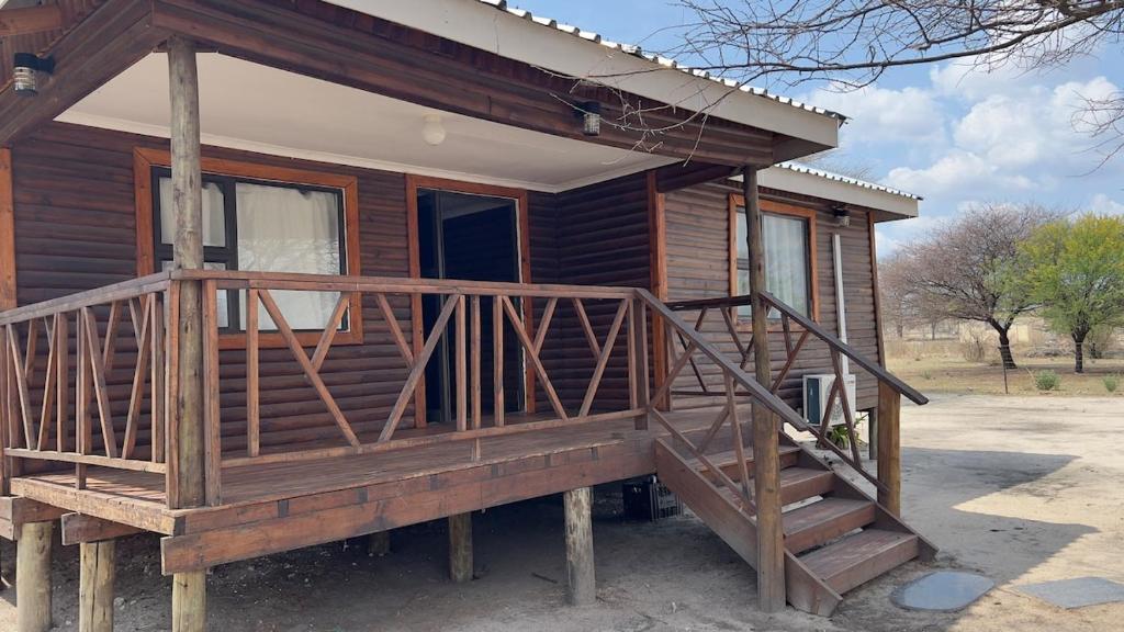 a log cabin with a large wooden porch and stairs at Maun HideOut in Maun Airport