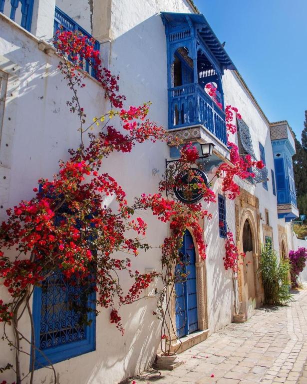 a white building with blue windows and red flowers at Maison Lella Kmar Sidi Bou said in Sidi Bou Saïd