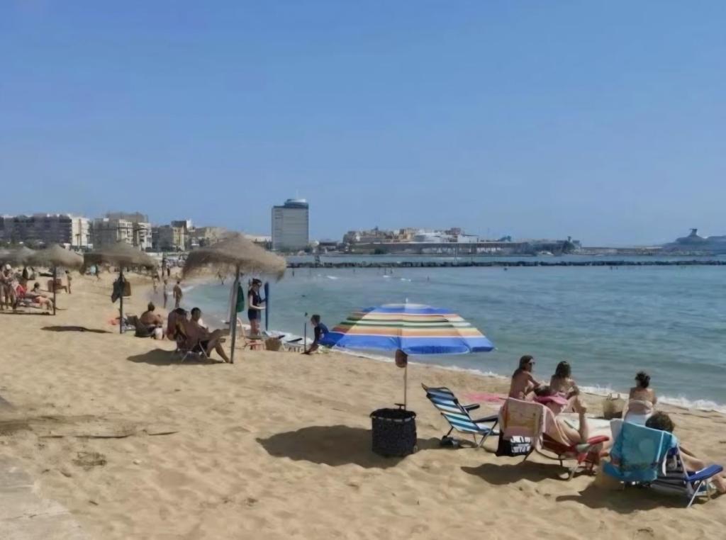 a group of people sitting on a beach with an umbrella at Loft paradisse in Melilla