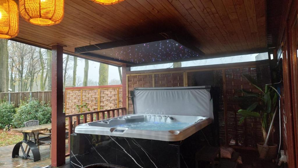 a hot tub sitting on a patio under a roof at Drents Genieten - Grasheide met Wellness in Erm
