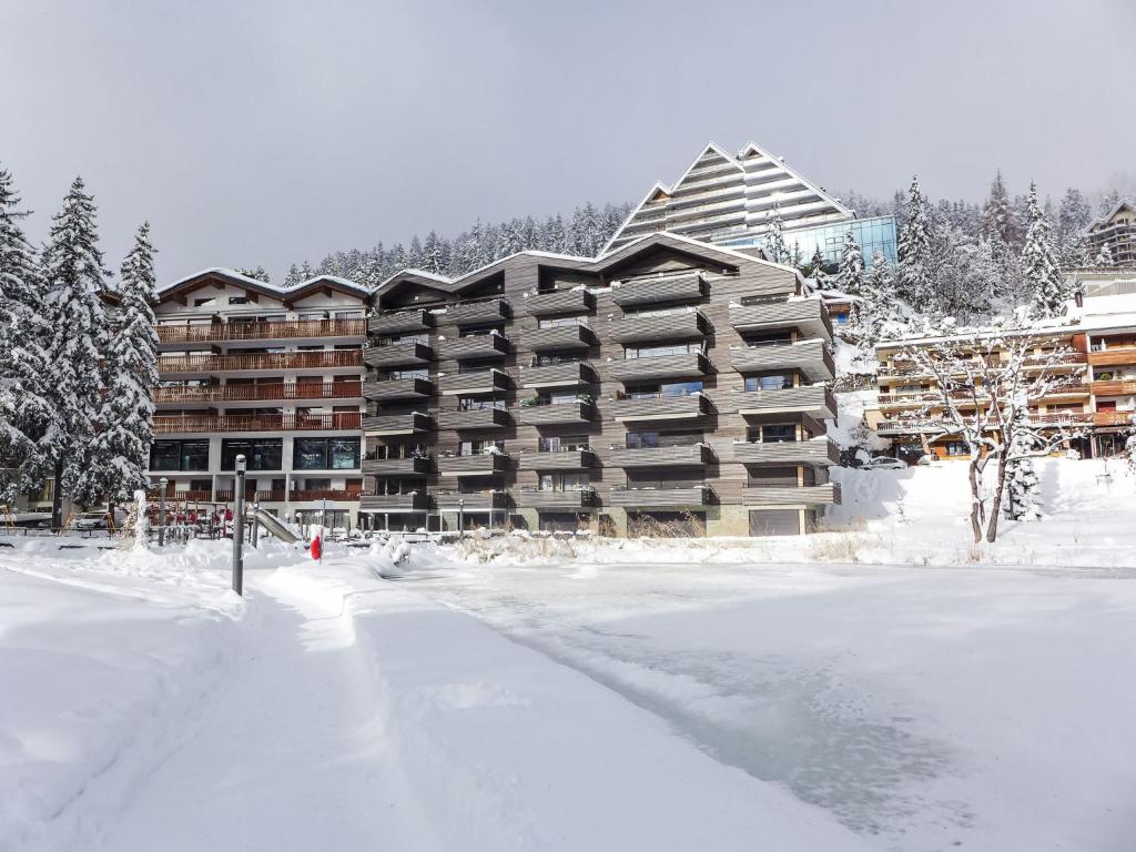 a large apartment building in the snow with a parking lot at Apartment Central Parc 2 by Interhome in Crans-Montana