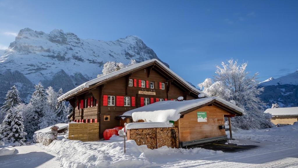 una casa cubierta de nieve con una montaña en el fondo en Naturfreunde Hostel Grindelwald, en Grindelwald