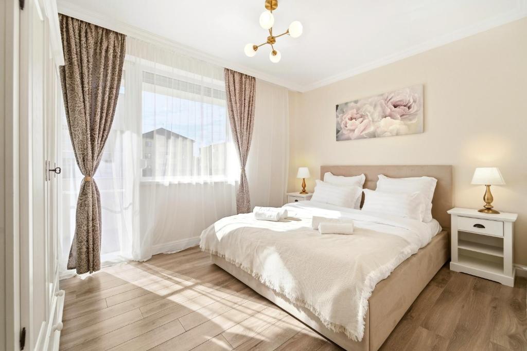 a white bedroom with a large bed and a window at Charming French Getaway Spacious Apartment with Garden and Parking in Dumbrăviţa