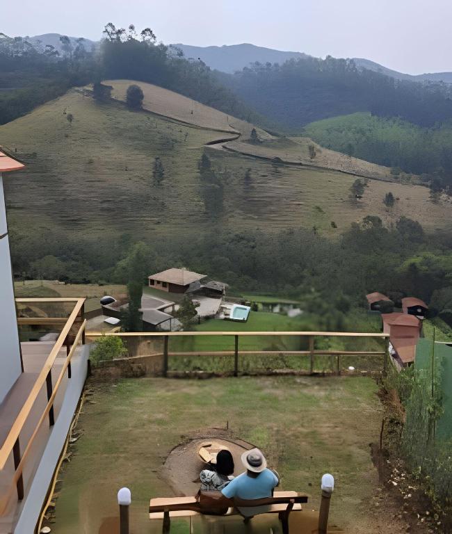 two people sitting on a bench looking at a mountain at Chalé com bela vista para as montanhas in Resende