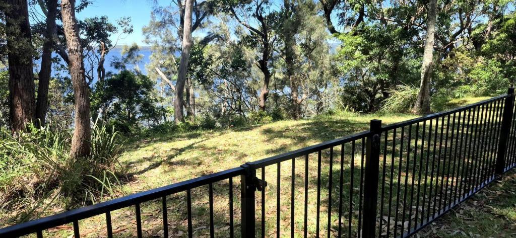 圣殿海岬Greville Getaway - Absolute Waterfront的山坡上有一道黑色栅栏，周围是树木和草地。