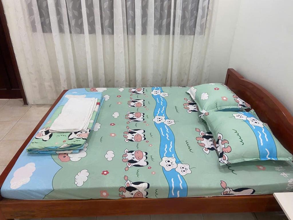 Phú MỹNha Nghi Phu Gia的一张床上铺着一条印有卡通动物图案的毯子。