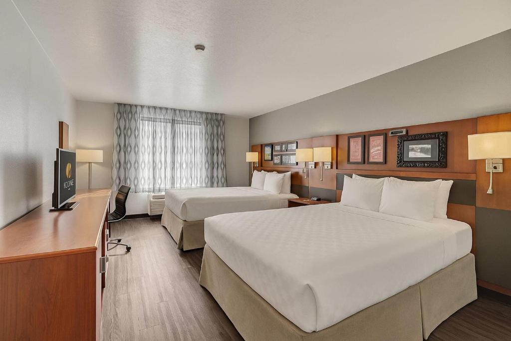a hotel room with two beds and a desk at Suburban Studios Salt Lake City Airport in Salt Lake City