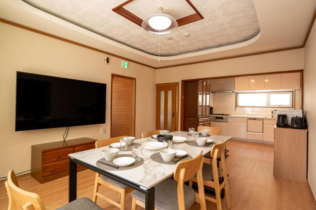 una sala da pranzo con un tavolo con sedie e una televisione di 緑の夢の家 a Furano