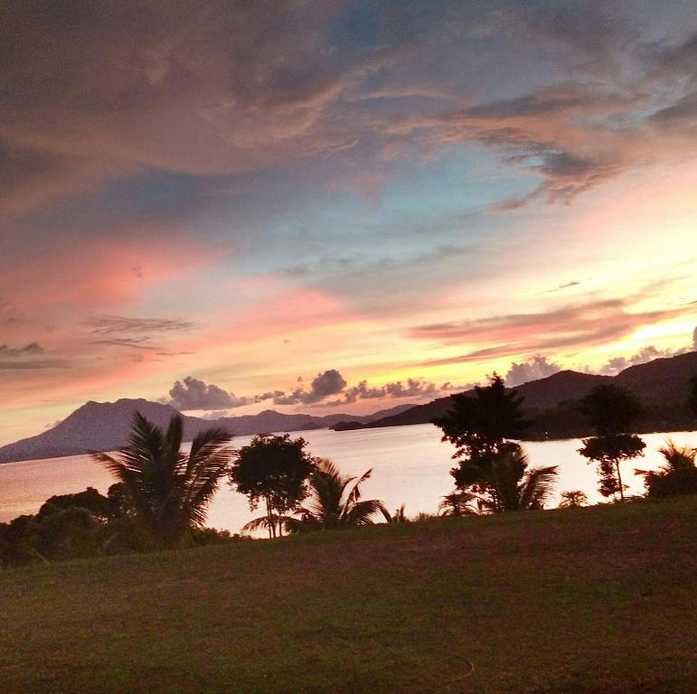 a sunset over a body of water with palm trees at Waddy Inn and Leisure Farm in Taytay