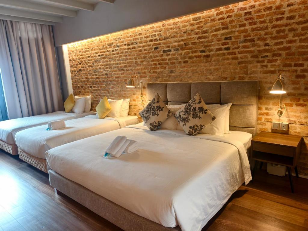 twee bedden in een kamer met een bakstenen muur bij Loke Thye Kee Heritage Hotel in George Town