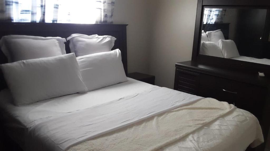 卡蒂马穆利洛Namasiku's Self Catering的一张带白色床单和枕头的床铺,位于镜子前