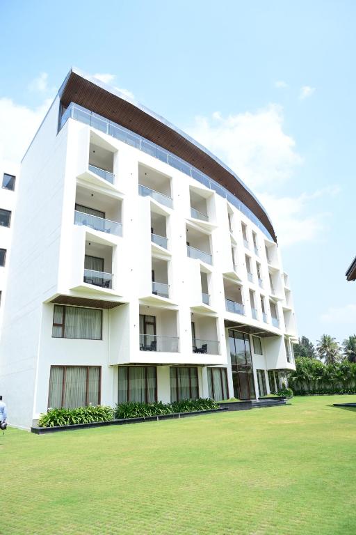 a white building with a grass field in front of it at IJ Crowne in Mysore