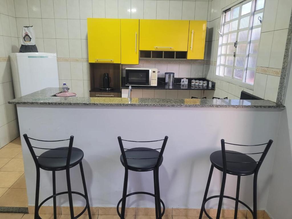 una cucina con tre sgabelli da bar e un bancone con mobili gialli di Casa á 5 minutos do Paraquedismo a Boituva