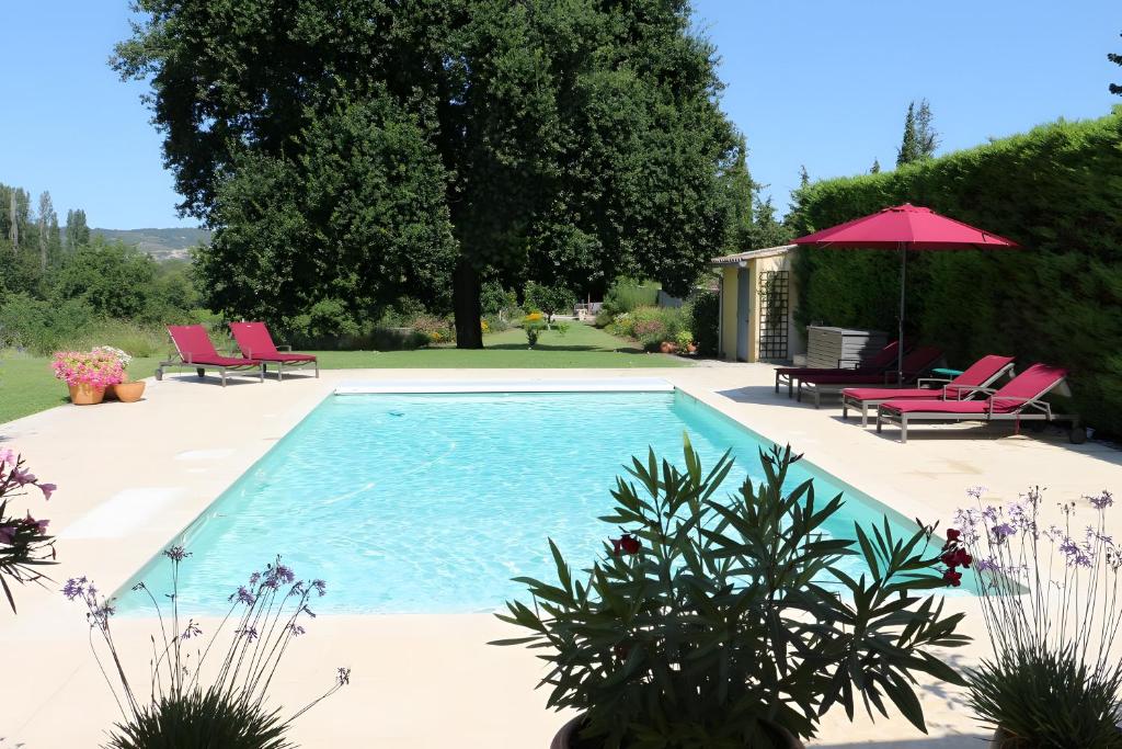 einen Pool mit rosa Stühlen und einem Sonnenschirm in der Unterkunft Chambre D'hôtes - Les Hirondelles in Mirabel-aux-Baronnies