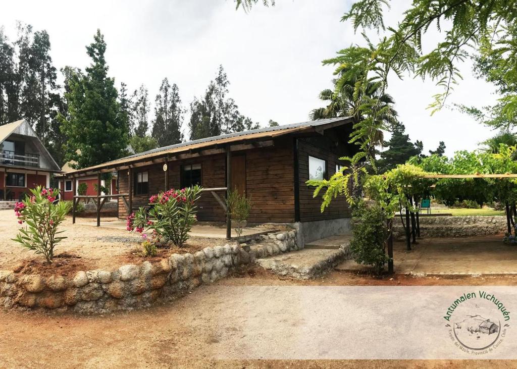 a wooden house with a stone wall in front of it at Cabañas Antumalen Vichuquén in Lago Vichuquen