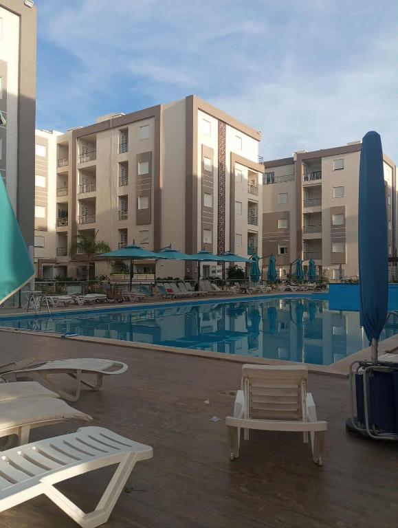 a swimming pool with chairs and umbrellas in front of buildings at Appartement Neuf au Bord de la Mer - Hammamet Sud Zone Touristique in Hammamet