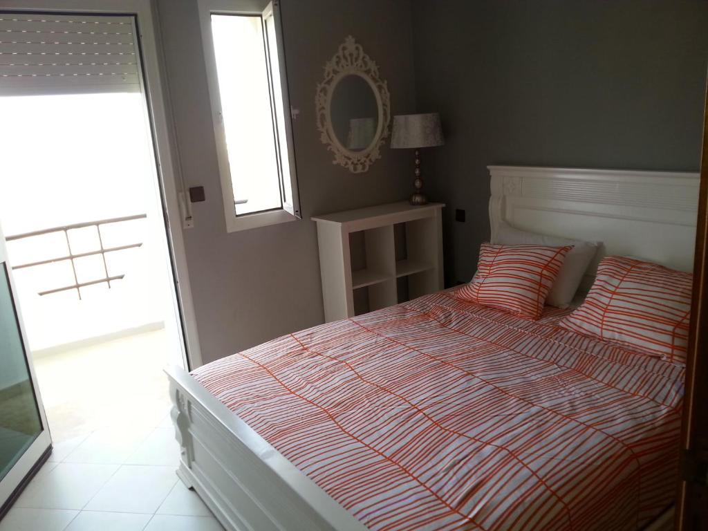 a bedroom with a bed and a window and a mirror at Apartment dans Residence avec piscine à Achakar in Jebila