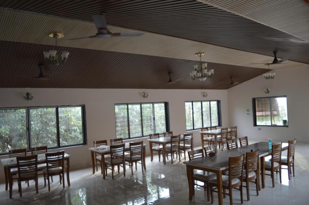 Nirvana Bhimashankar Jungle Resort في بهيماشانكار: غرفة طعام مع طاولات وكراسي ونوافذ