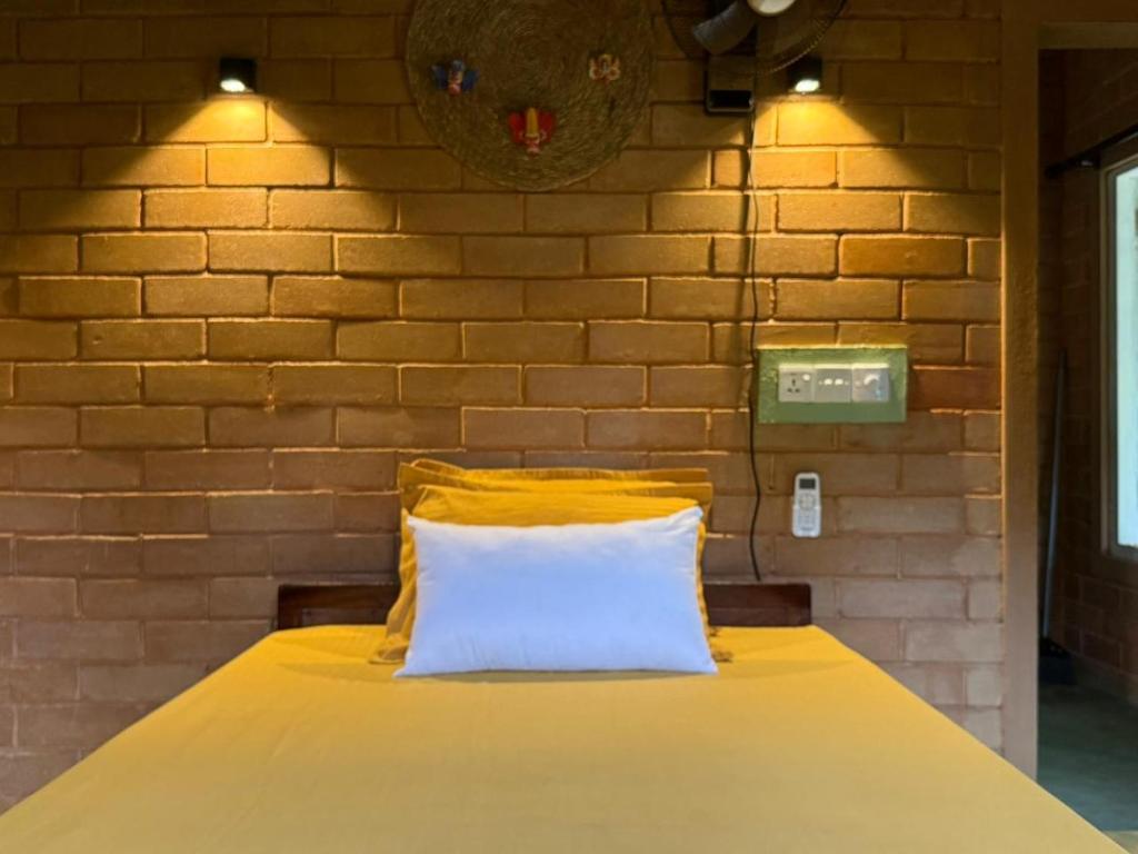 een bed met een geel kussen en een bakstenen muur bij Eco Bricks in Ahangama