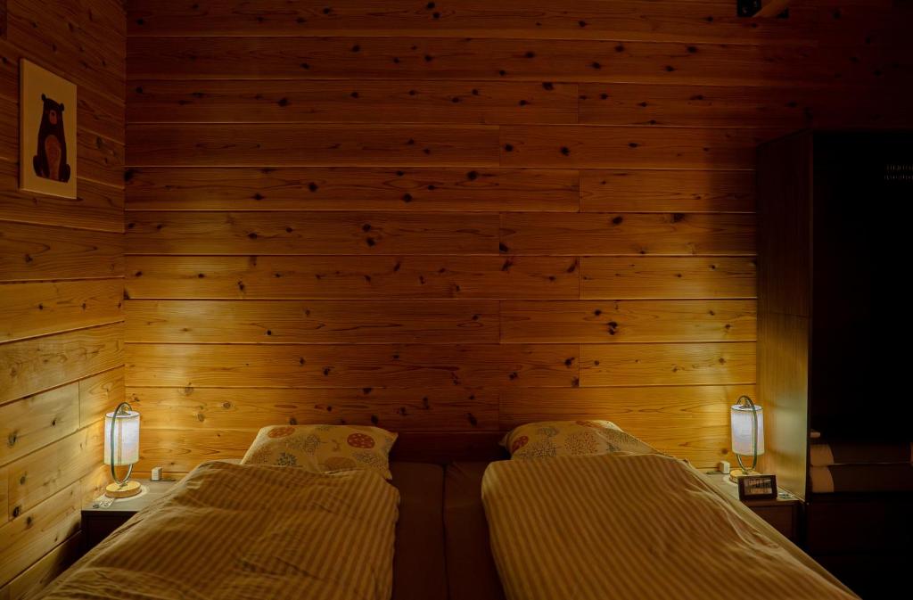 安昙野市Azumino Bear's Inn的一间木墙房间里有两张床