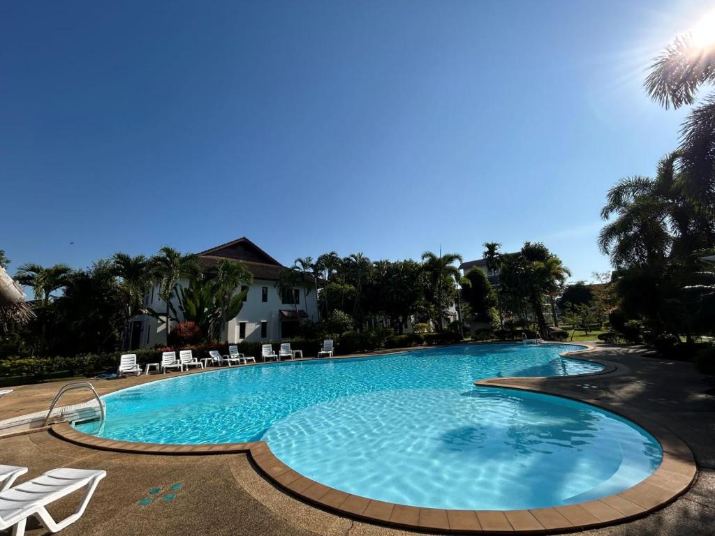 a large blue swimming pool with chairs and trees at Teak Garden Resort, Chiang Rai in Chiang Rai