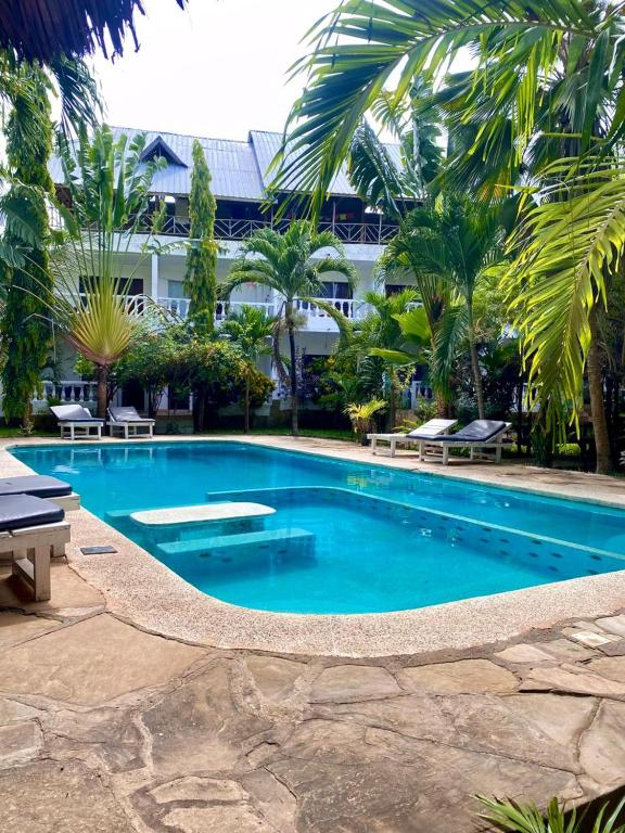 a large swimming pool in a resort with palm trees at MALKIA SUITEs in Diani Beach