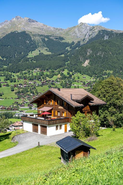 a large house on a hill with mountains in the background at Chalet Studen in Grindelwald