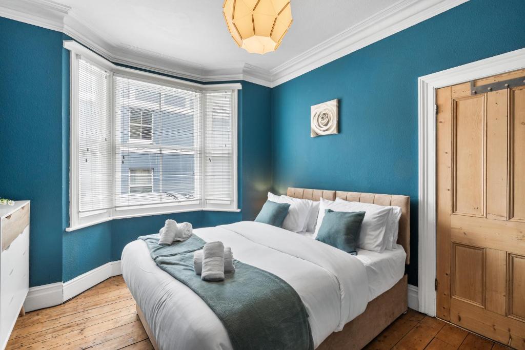 a blue bedroom with a bed and two windows at The Quirk & Timber Retreat with Free parking in Brighton & Hove