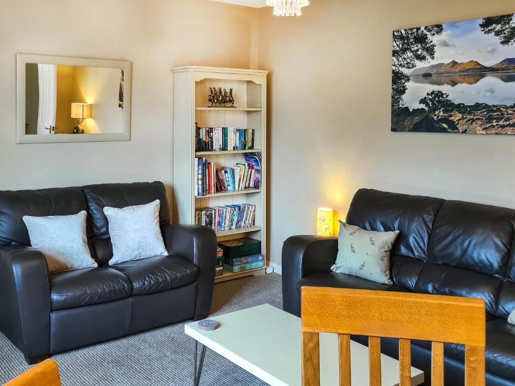 een woonkamer met een zwarte leren bank en een boekenplank bij 10 Elm Court in Keswick
