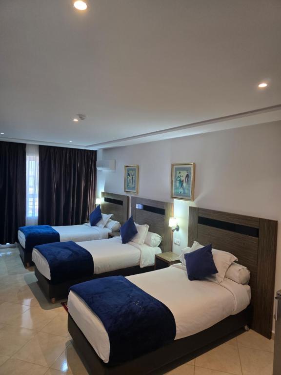 a hotel room with three beds with blue pillows at Tanger Med Hotel, Conference & Catering in Ghdar Defla