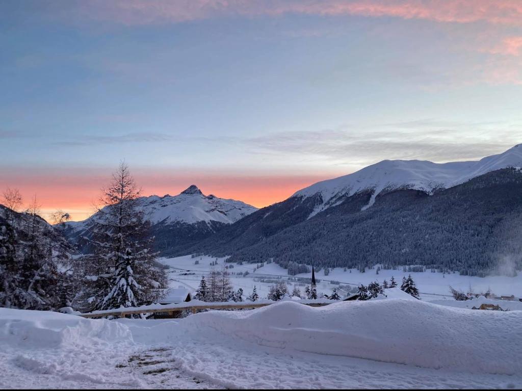 a snowy mountain range with a sunset in the background at Kleines aber feines Studio in Zuoz