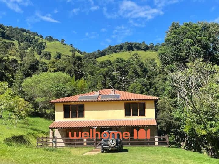 una casa con un cartello di benvenuto in un campo di Chale Manticas Blue na Serra da Mantiqueira a Córrego do Bom Jesus
