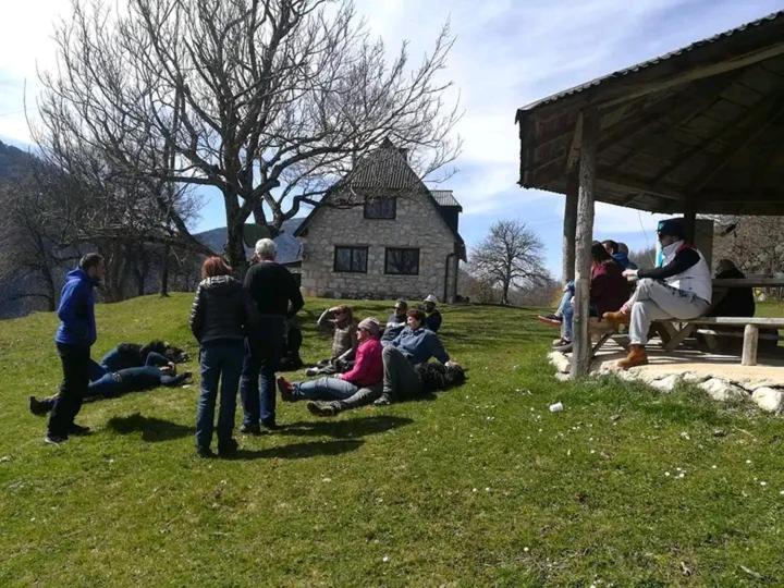 a group of people sitting in the grass near a house at Camp Apartmani Tara in Pljevlja