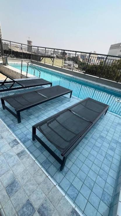 a swimming pool with two benches and a table at Studio Metrô Tucuruvi in São Paulo