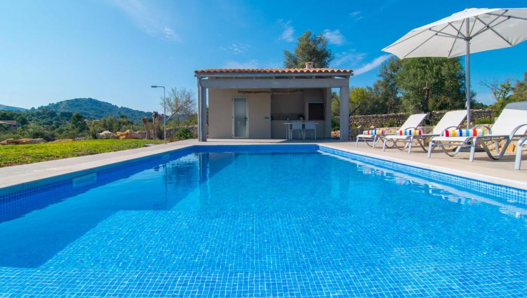a pool with chairs and an umbrella next to a house at Can Colomer Ferragut in Artá