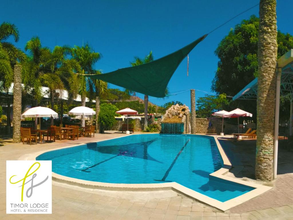 una piscina en un complejo con mesas y sombrillas en Timor Lodge, en Dili