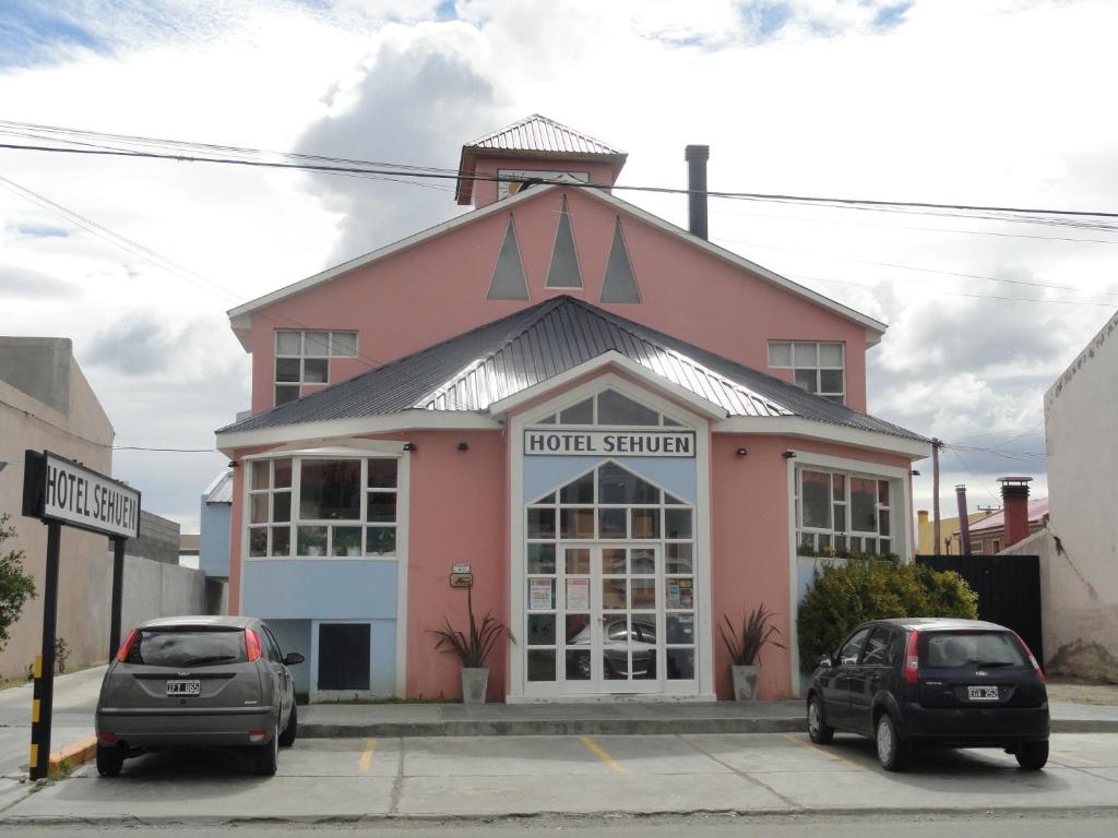 różowy budynek z samochodami zaparkowanymi przed nim w obiekcie Hotel Sehuen w mieście Río Gallegos