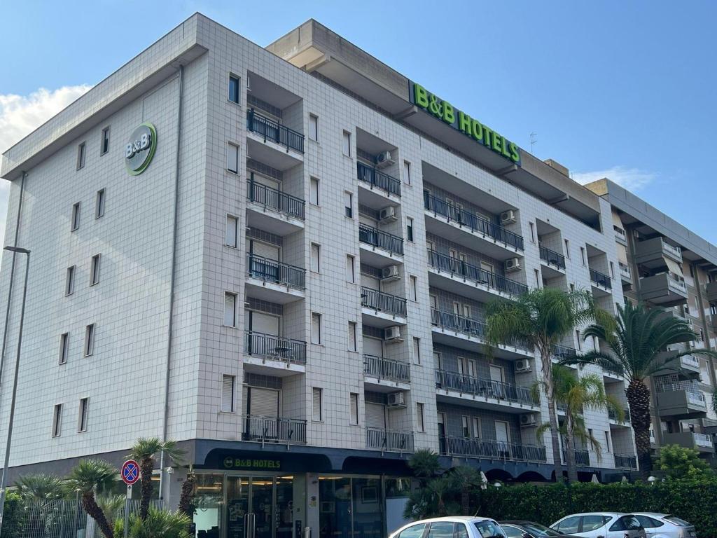 B&B HOTEL Bari Rondò في باري: مبنى أبيض كبير مع سيارات متوقفة أمامه