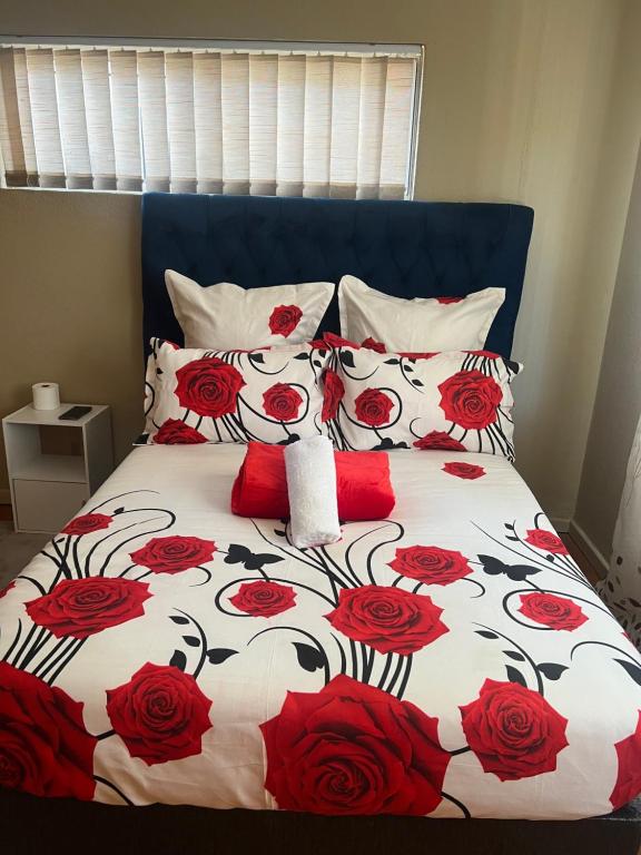 a bed with a red and white bedspread with red roses at Ridah's Accomodation in Bellville