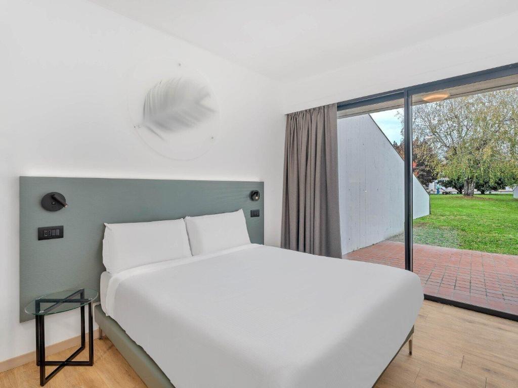 a bedroom with a white bed and a large window at B&B HOTEL Alba in Alba